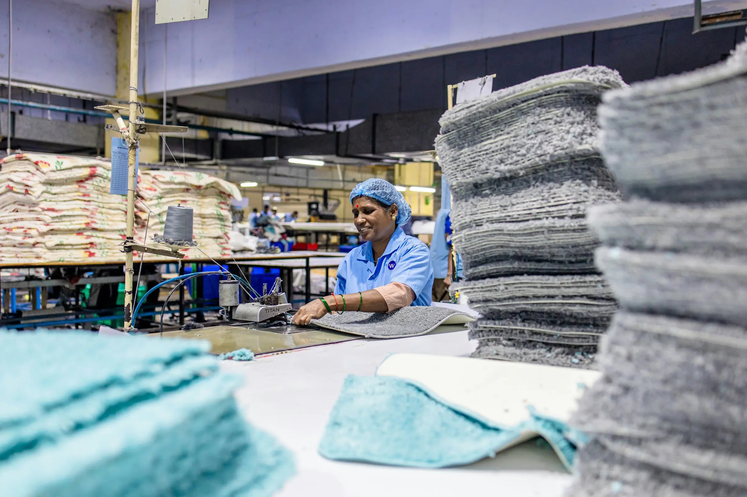 Woman in blue uniform and hairnet sewing grey textiles with a TITAN machine in a factory setting