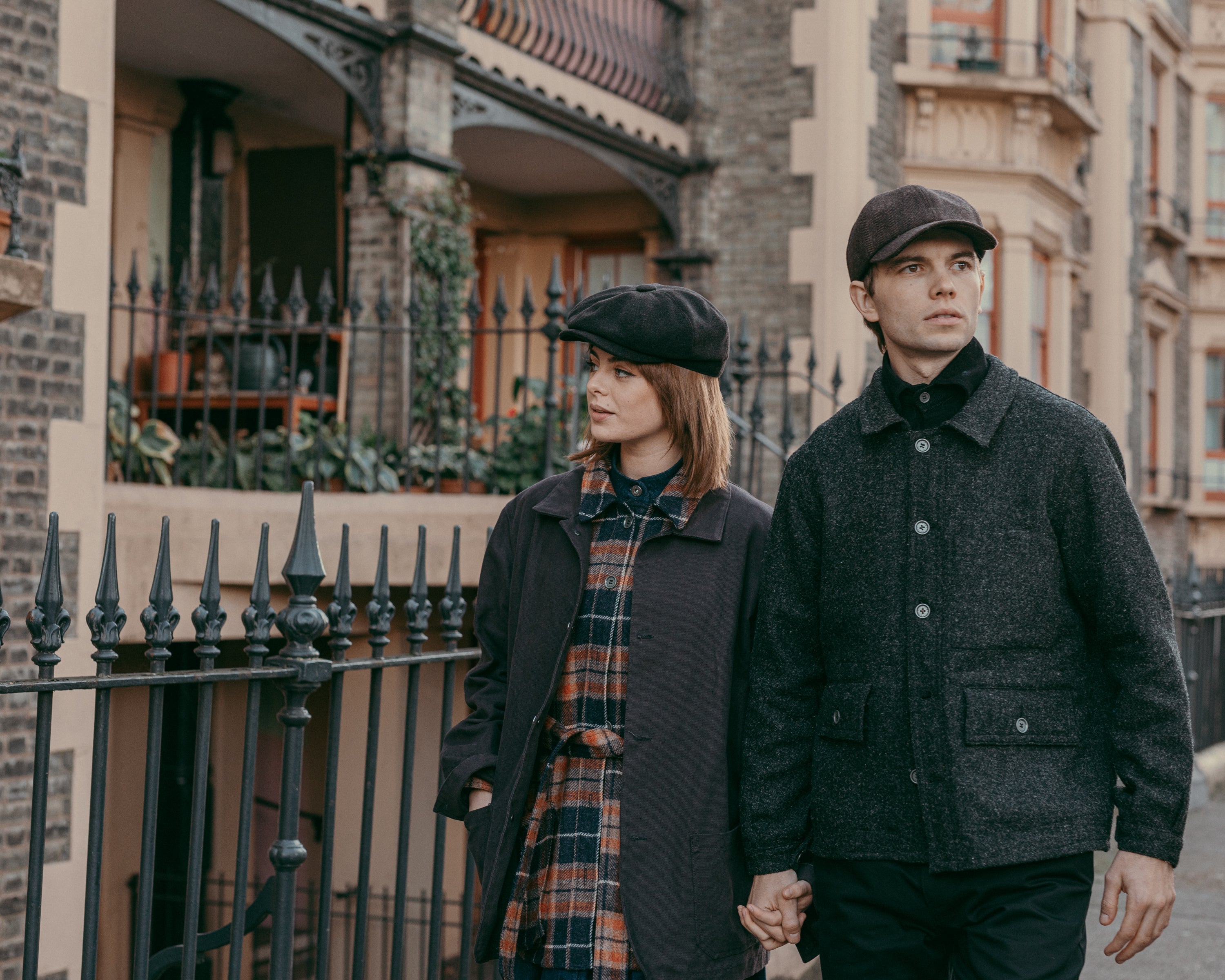 Young man and woman holding hands wearing dark wool coats and matching flat caps on an urban street