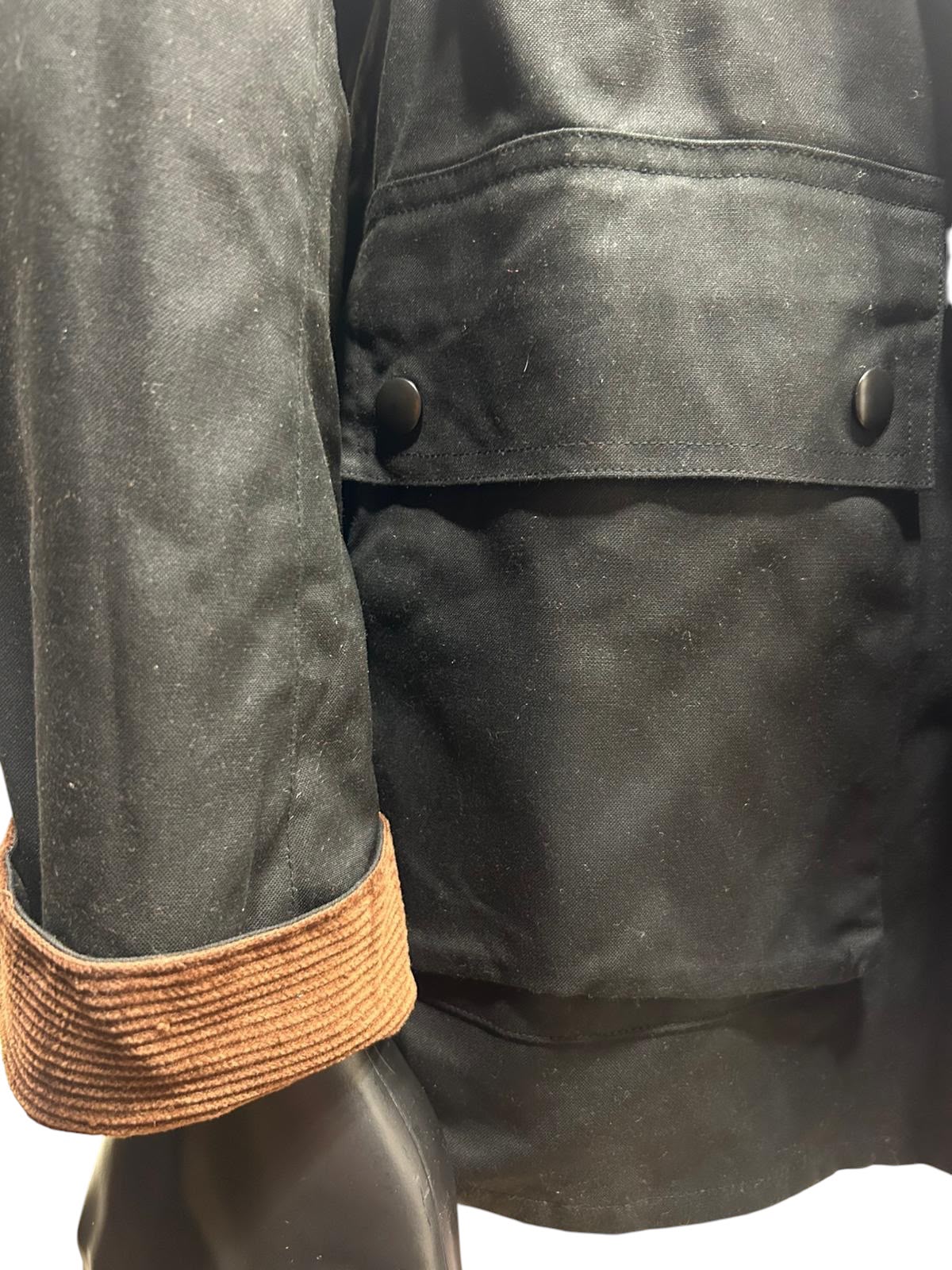 Close-up of black jacket sleeve with brown corduroy cuff and body flap secured by black snap buttons
