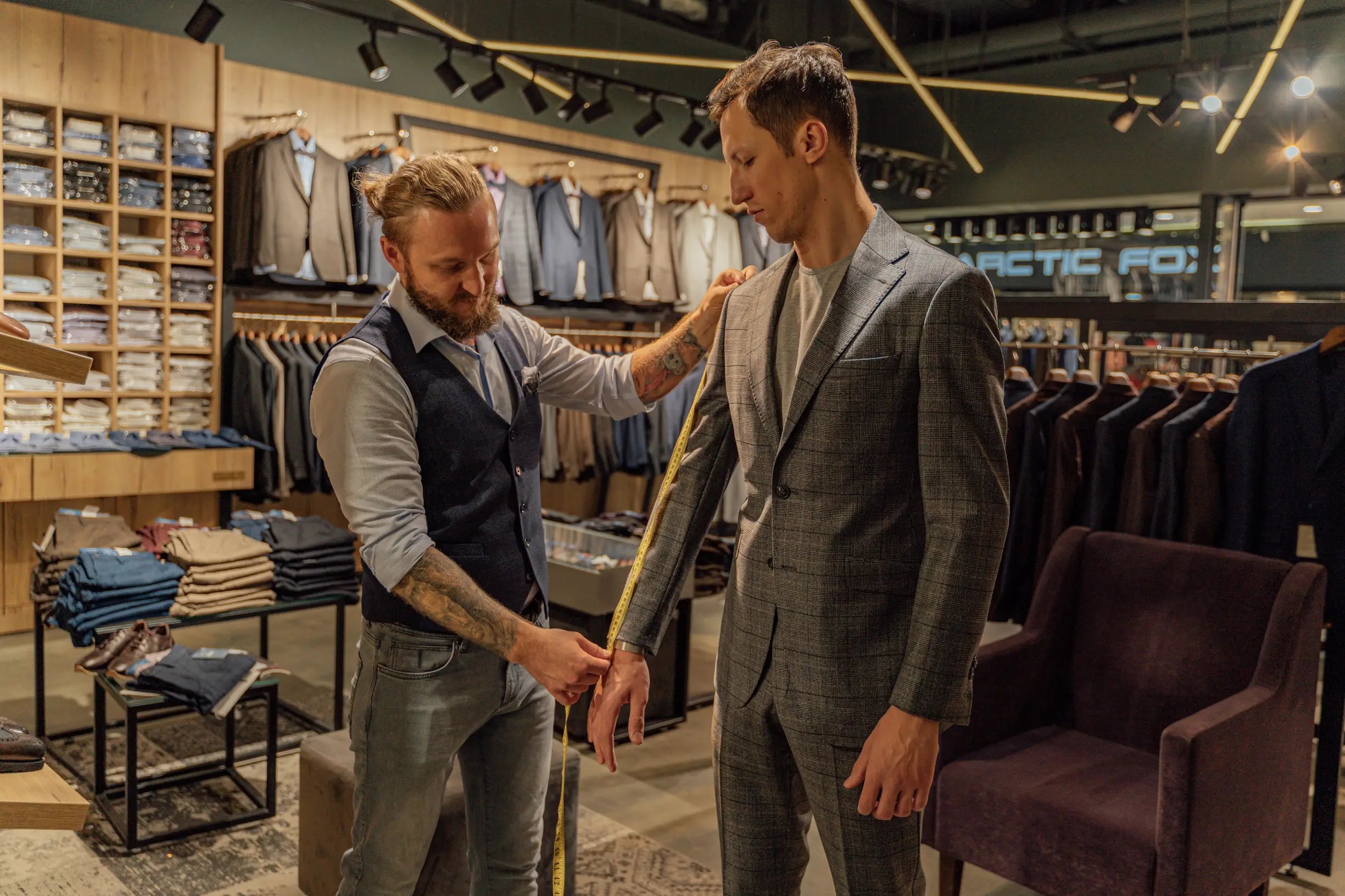 Tailor measuring sleeve length of man in gray plaid suit jacket inside clothing store
